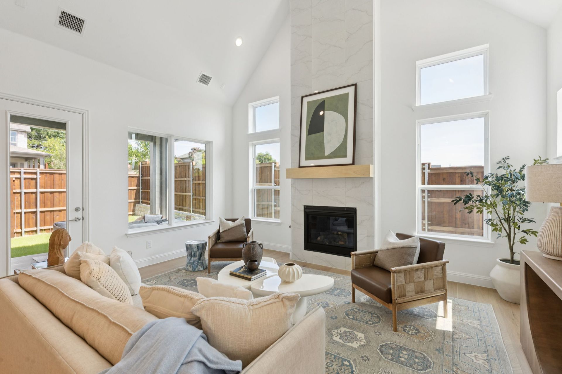 Bright, airy living room with high ceilings, fireplace, and large windows; furnished with neutral tones and modern decor.