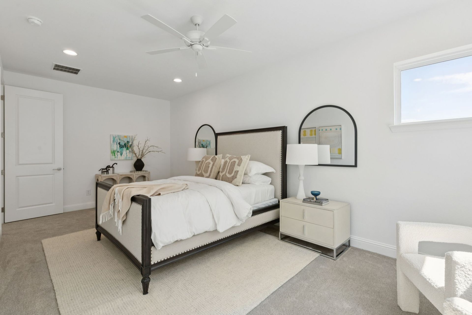 Bedroom with white walls, beige carpet, bed with linen headboard, and a mirror.