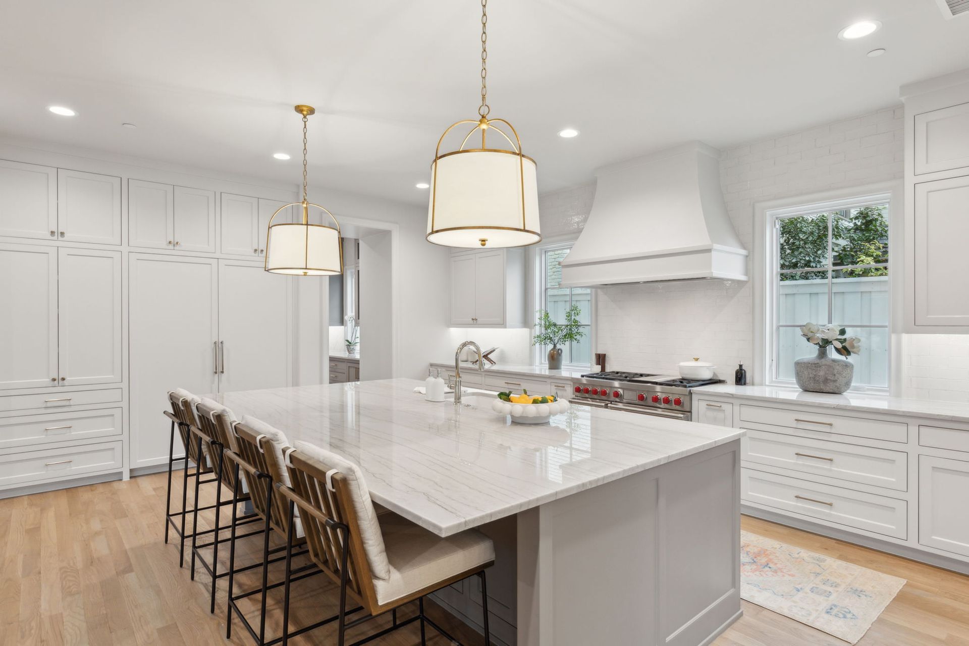 Spacious white kitchen with marble island, gold pendant lights, and bar stools.