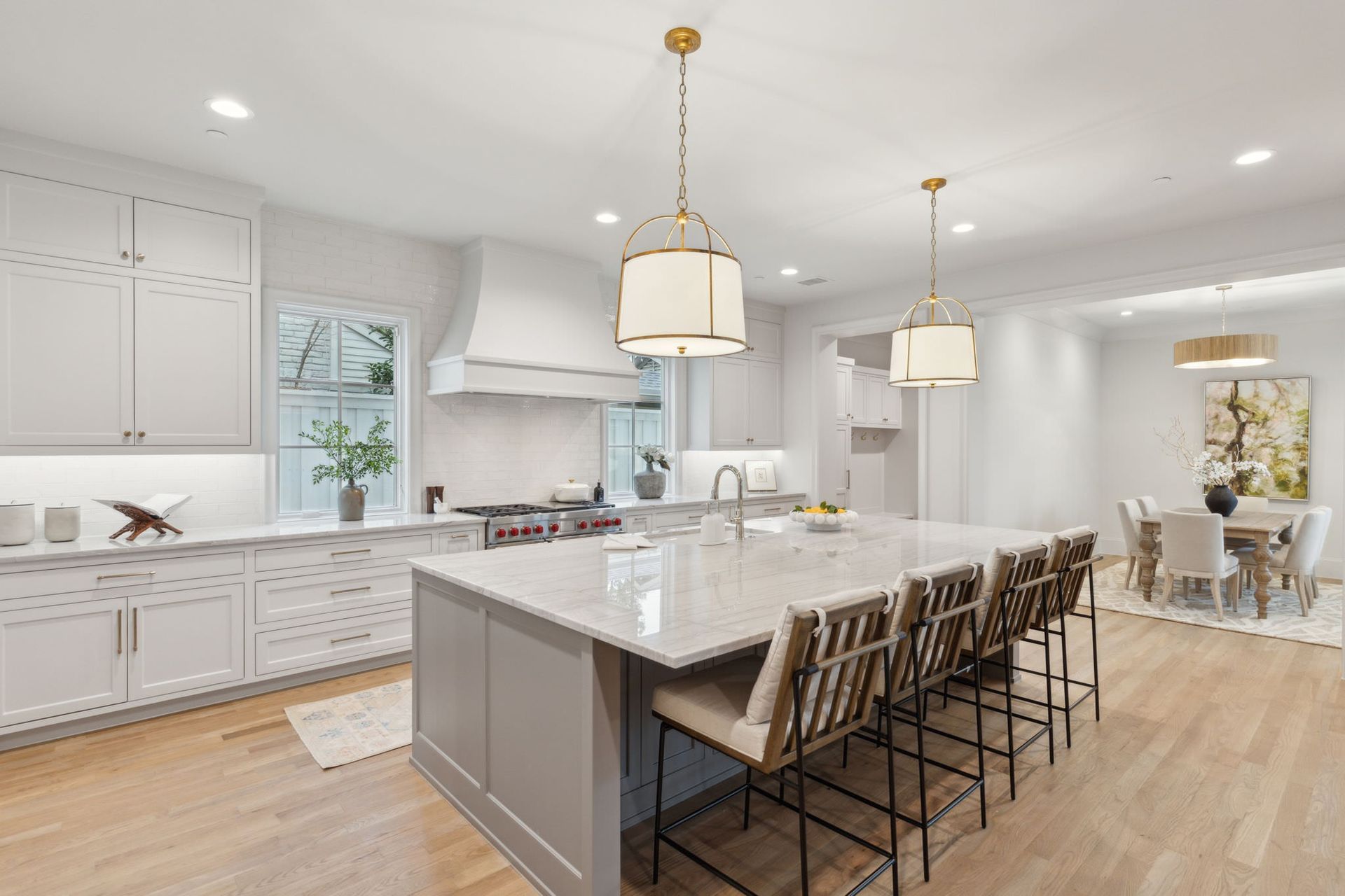 Modern white kitchen with island and light wood floors. Grey island with seating, light fixtures.
