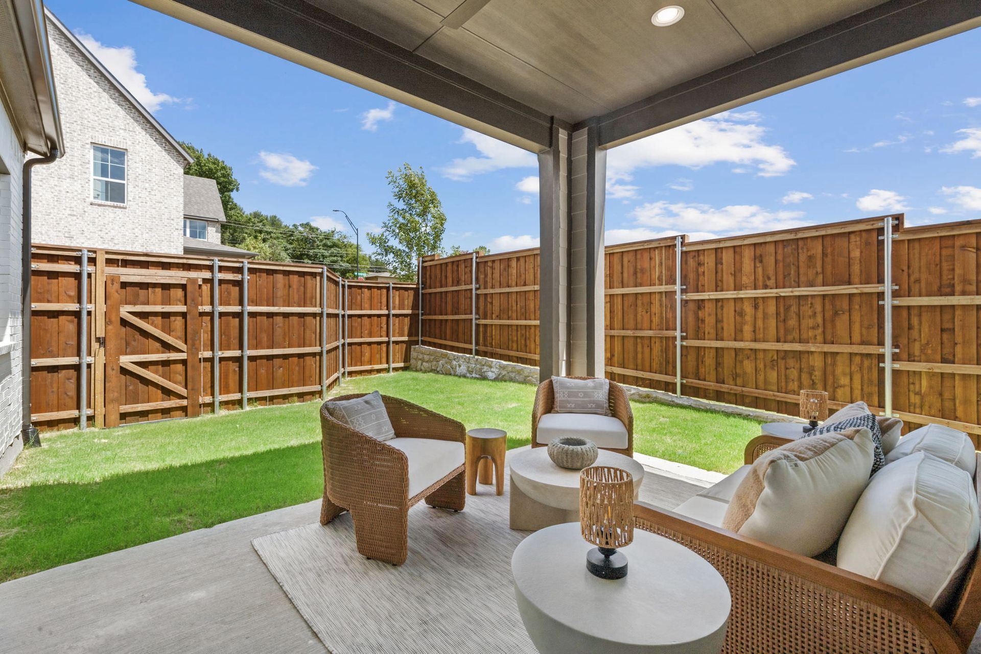 Patio with wicker furniture, a rug, and a small table. A fenced backyard is visible with a sunny blue sky.