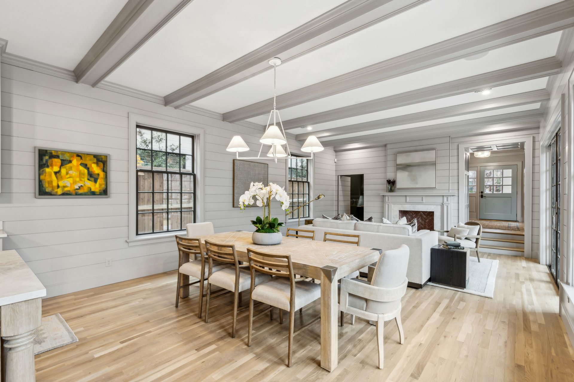 A dining room with a wooden table and chairs, gray walls, and wood floors, leading to a living room.