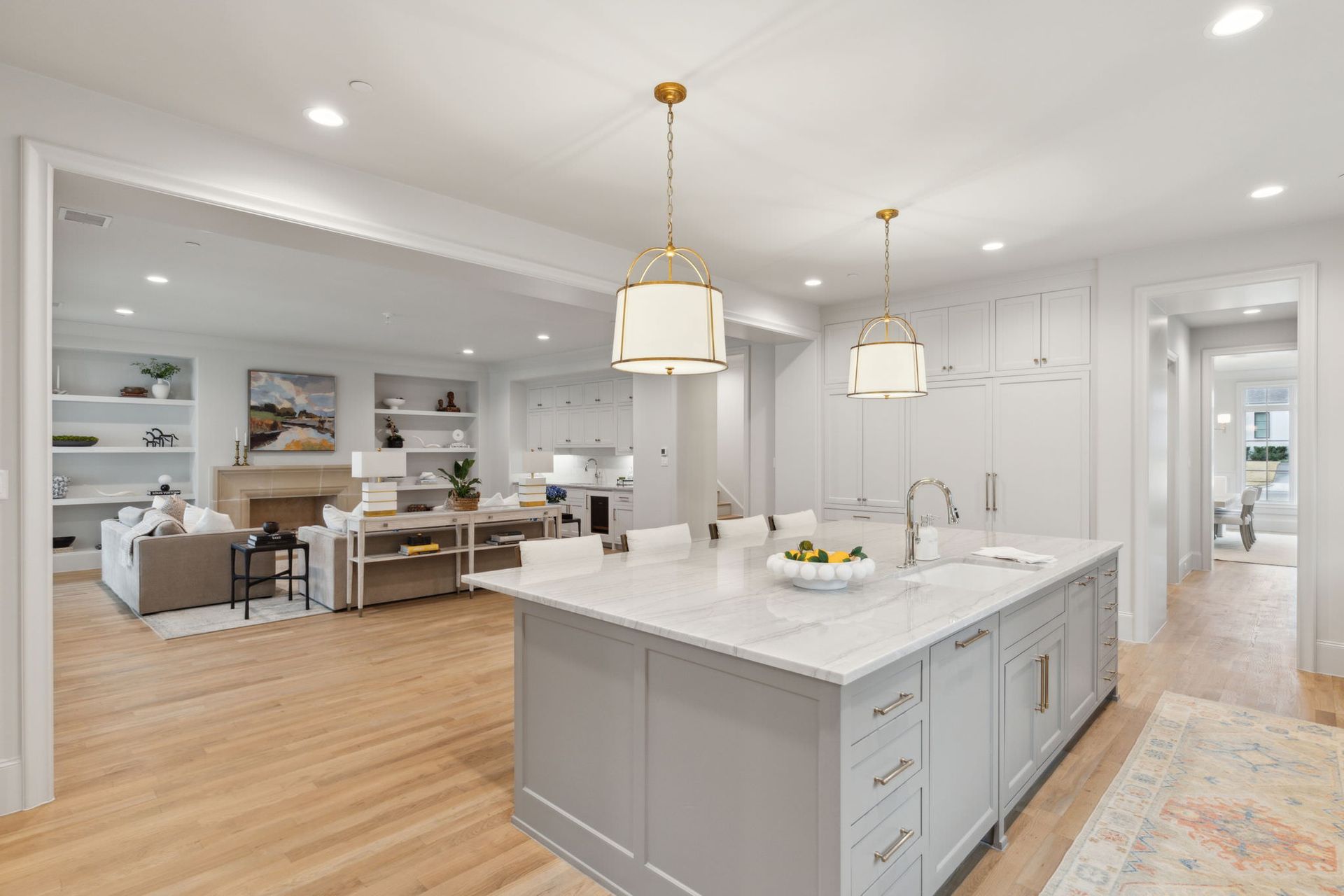 Open-concept kitchen with island, gray cabinets, and marble countertop. Living room in the background.