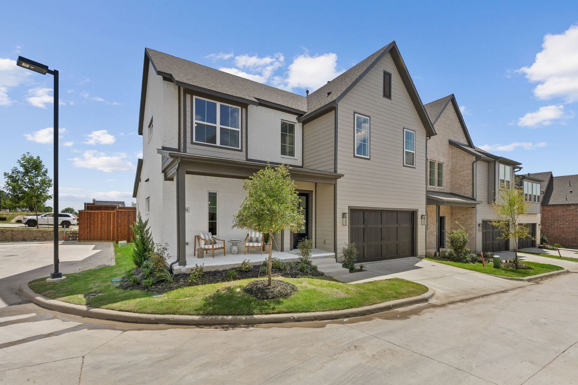 Modern townhome exteriors with a small front porch, green grass, and blue sky.