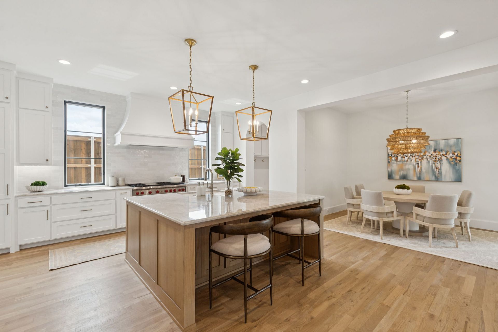 Spacious kitchen with island, wooden cabinets, marble countertops, gold pendant lights, and a dining area.