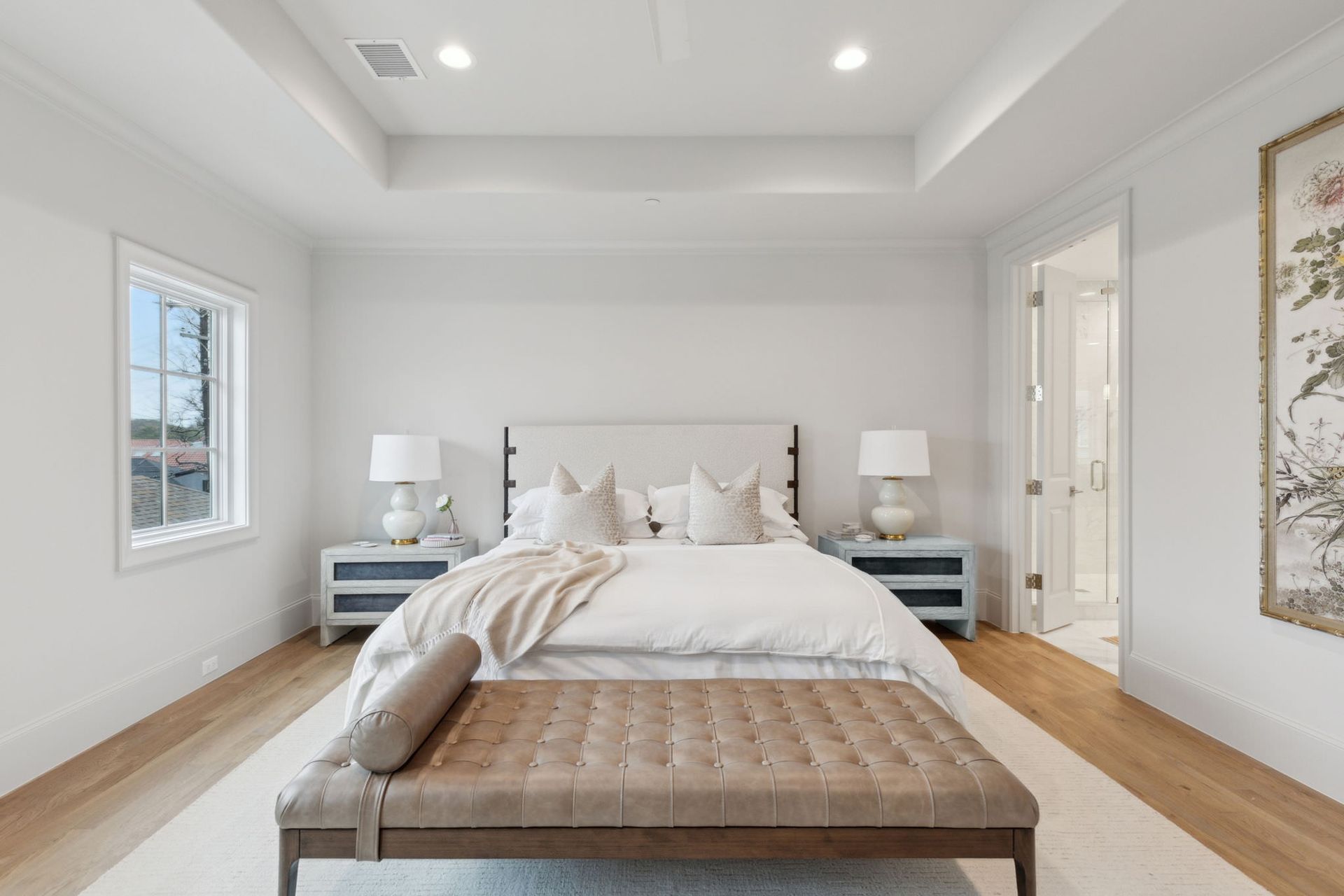 Bedroom with white walls, light wood floor, king bed, light blue nightstands, and a bench.