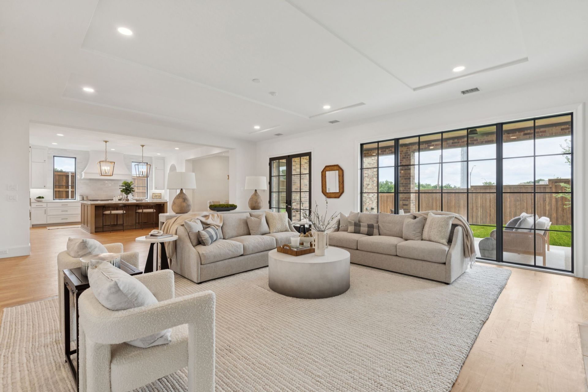 Spacious, bright living room with sofas, chairs, and a large rug. Open to a kitchen and outdoor patio.