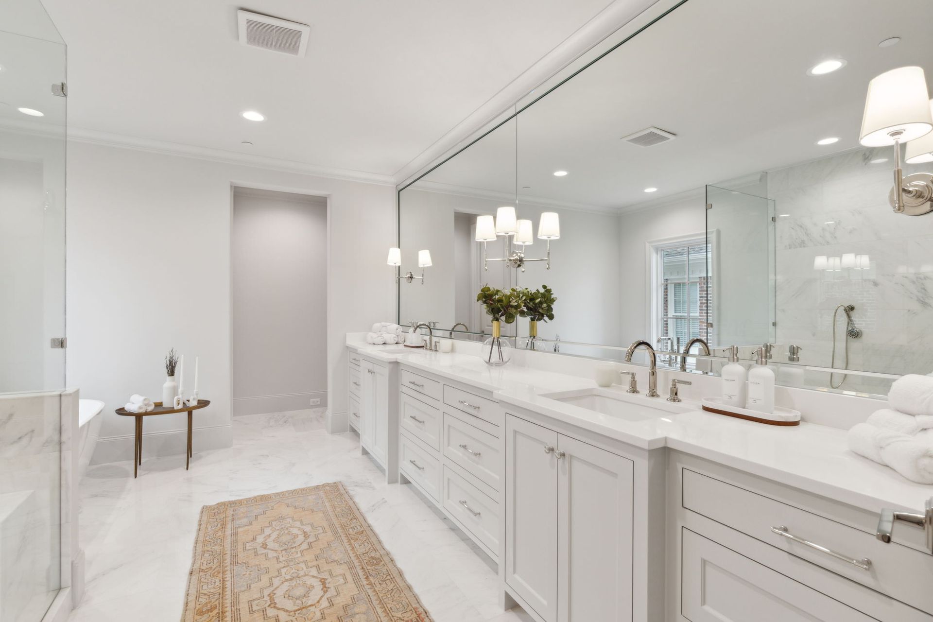 White modern bathroom with long vanity, large mirror, and marble tile.