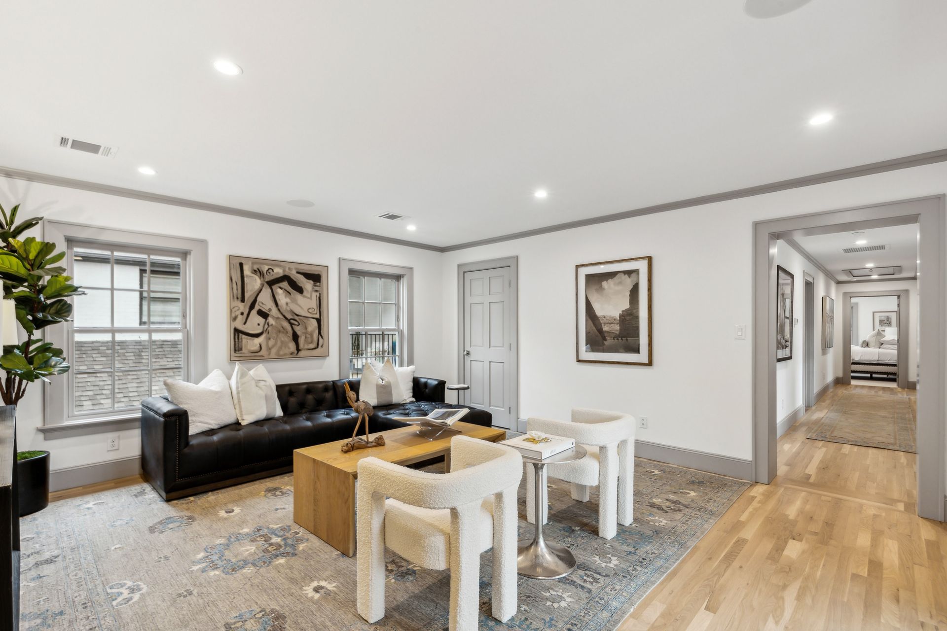 Living room with black sofa, beige chairs, art, and a doorway to a hallway.