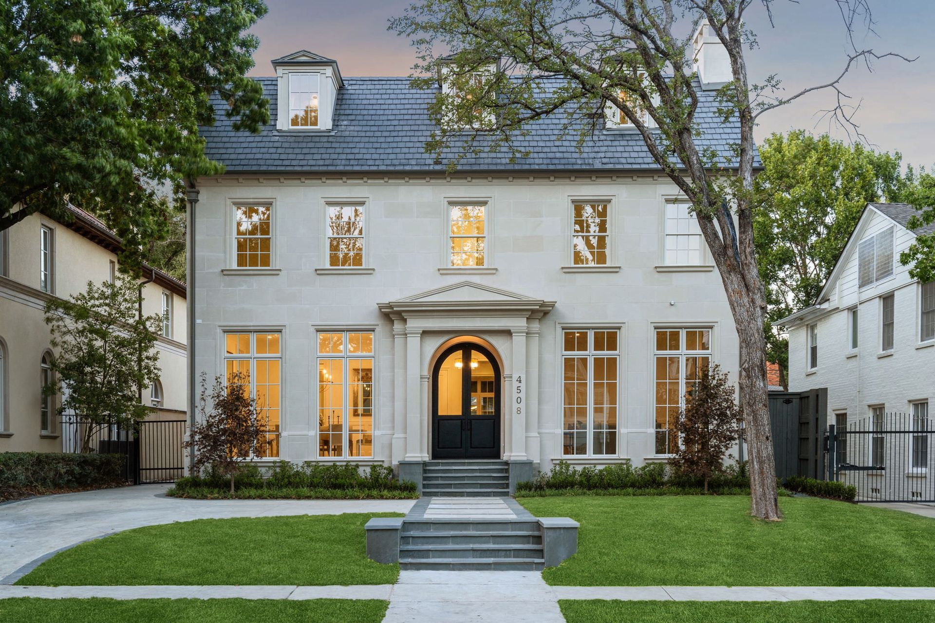 Two-story white house with arched doorway, gray roof, and manicured lawn.
