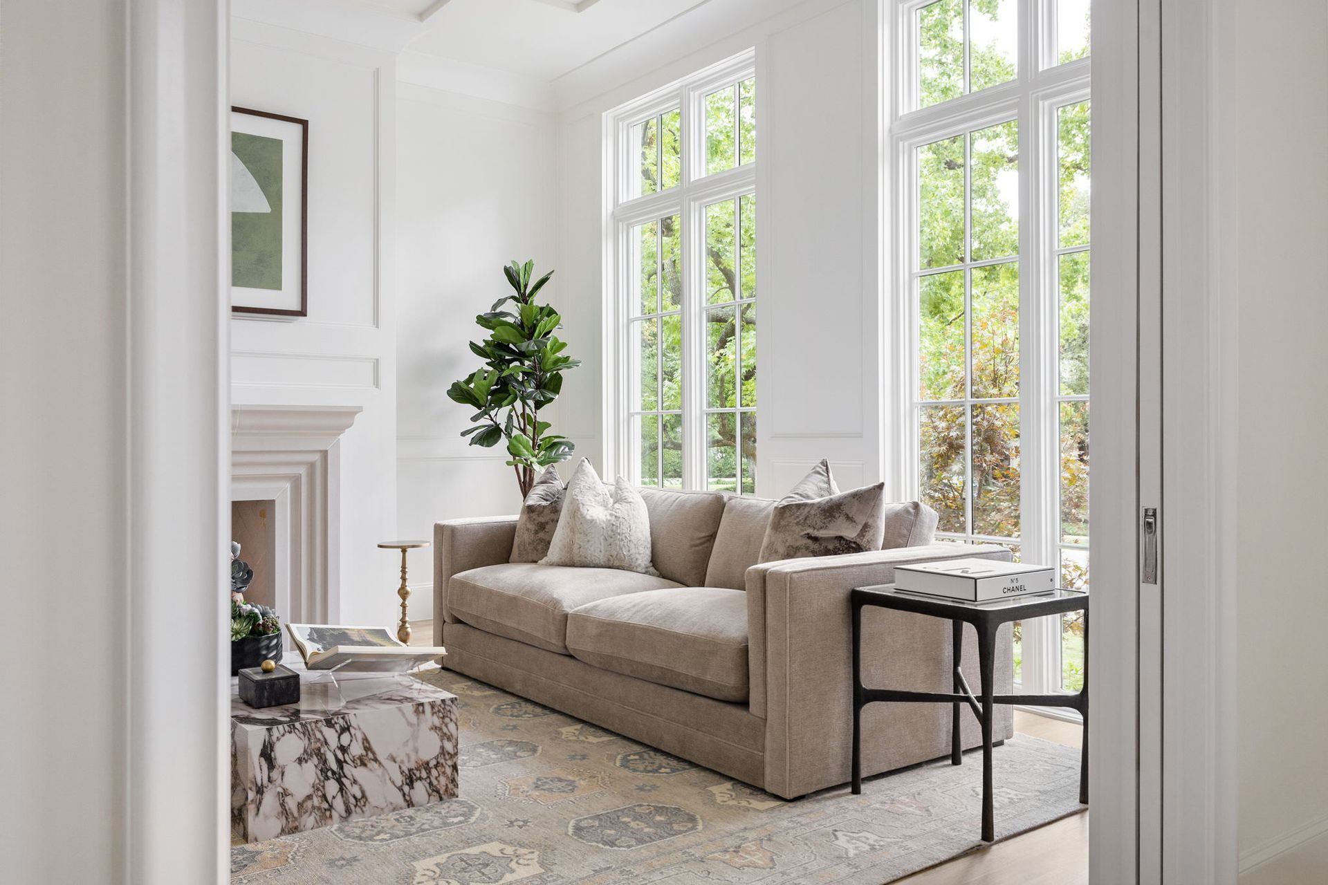 A living room with a couch , coffee table , fireplace and lots of windows.