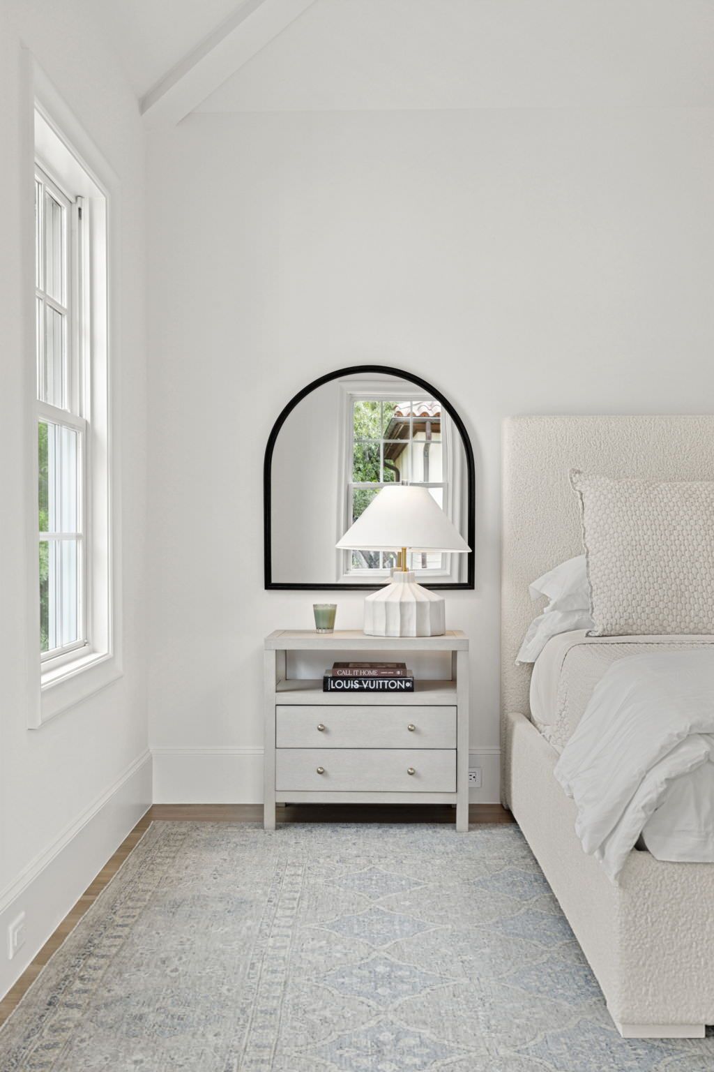 A bedroom with a bed , nightstand , mirror and window.