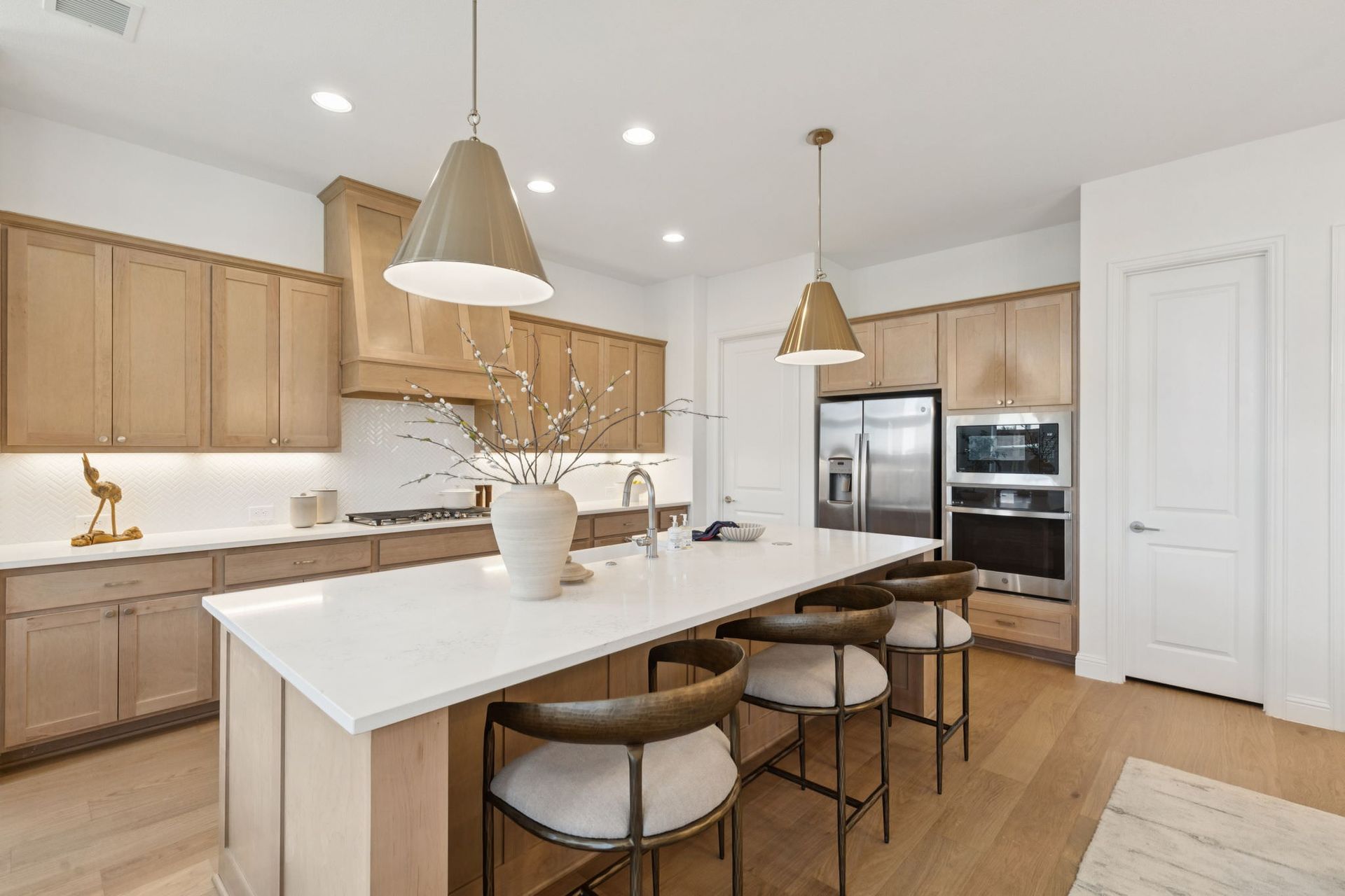 Modern kitchen with a large island, light wood cabinets, stainless steel appliances, and pendant lights.