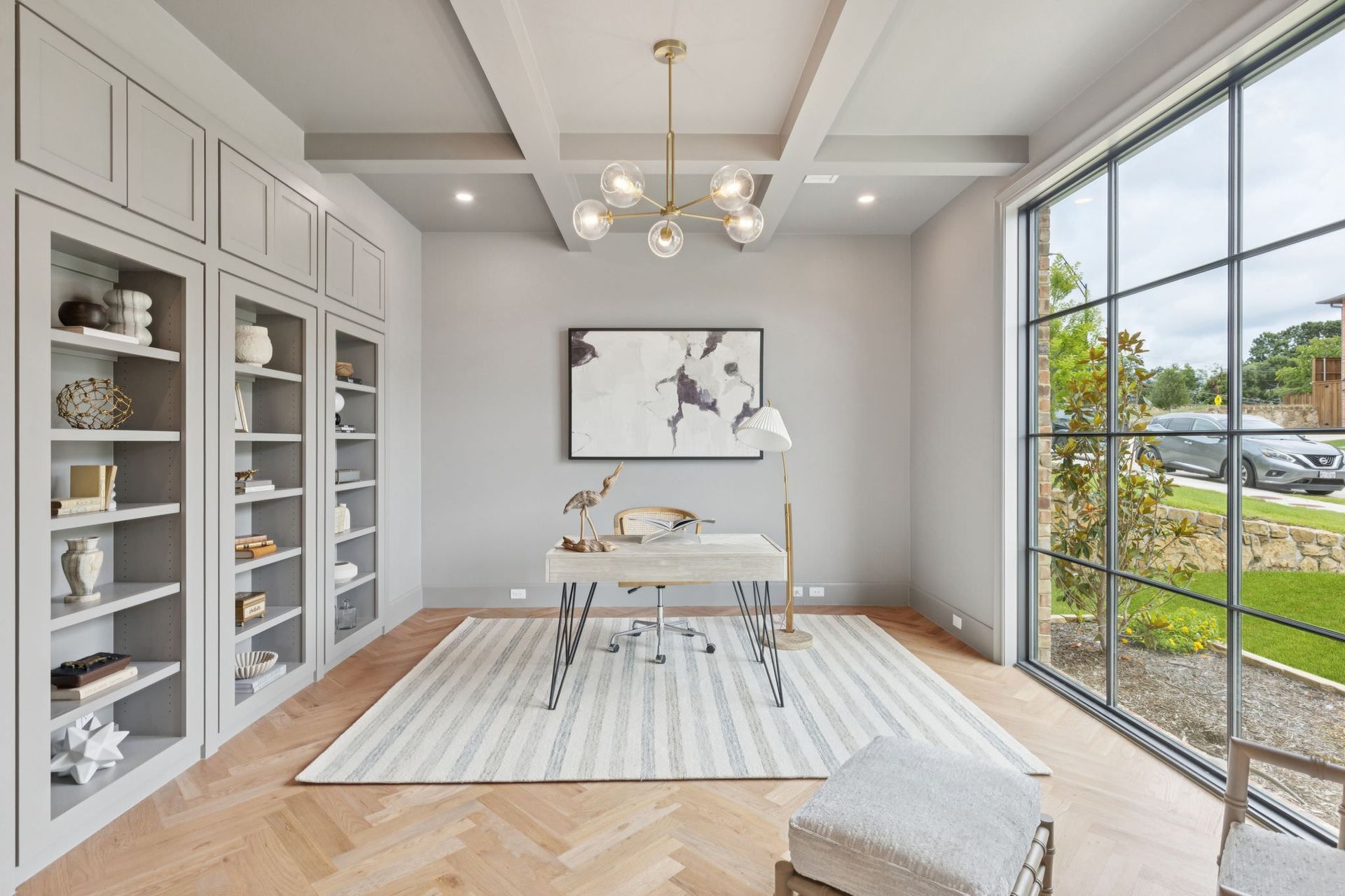 Home office with built-in bookshelves, large window, desk, and a light-colored rug on hardwood floors.