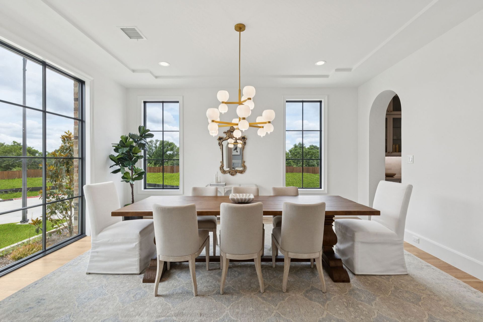 Formal dining room with large windows, wooden table, and chandelier; neutral colors.