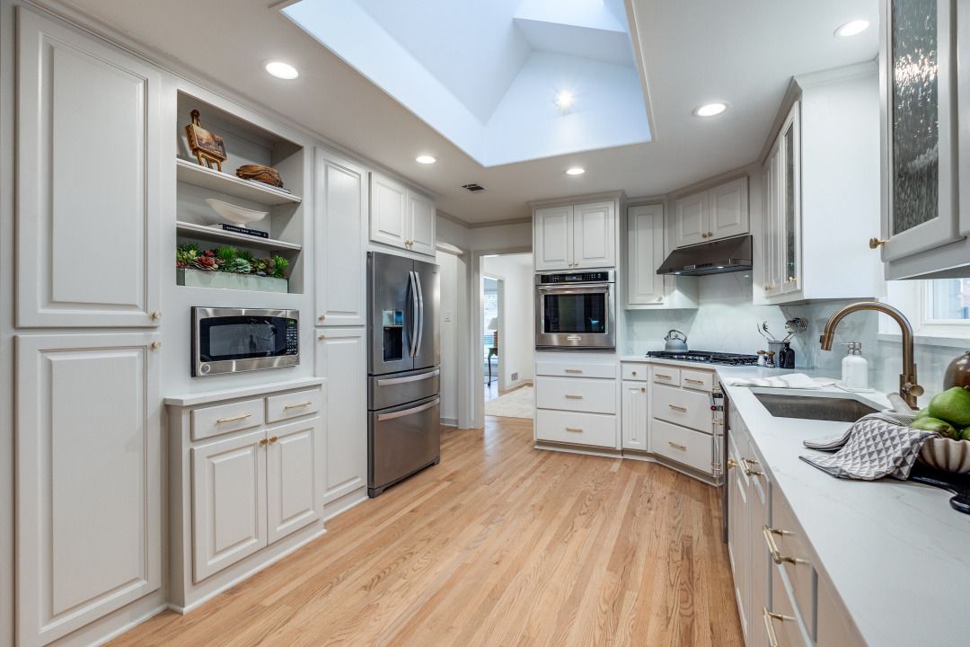 A kitchen with white cabinets , hardwood floors , stainless steel appliances and a skylight.
