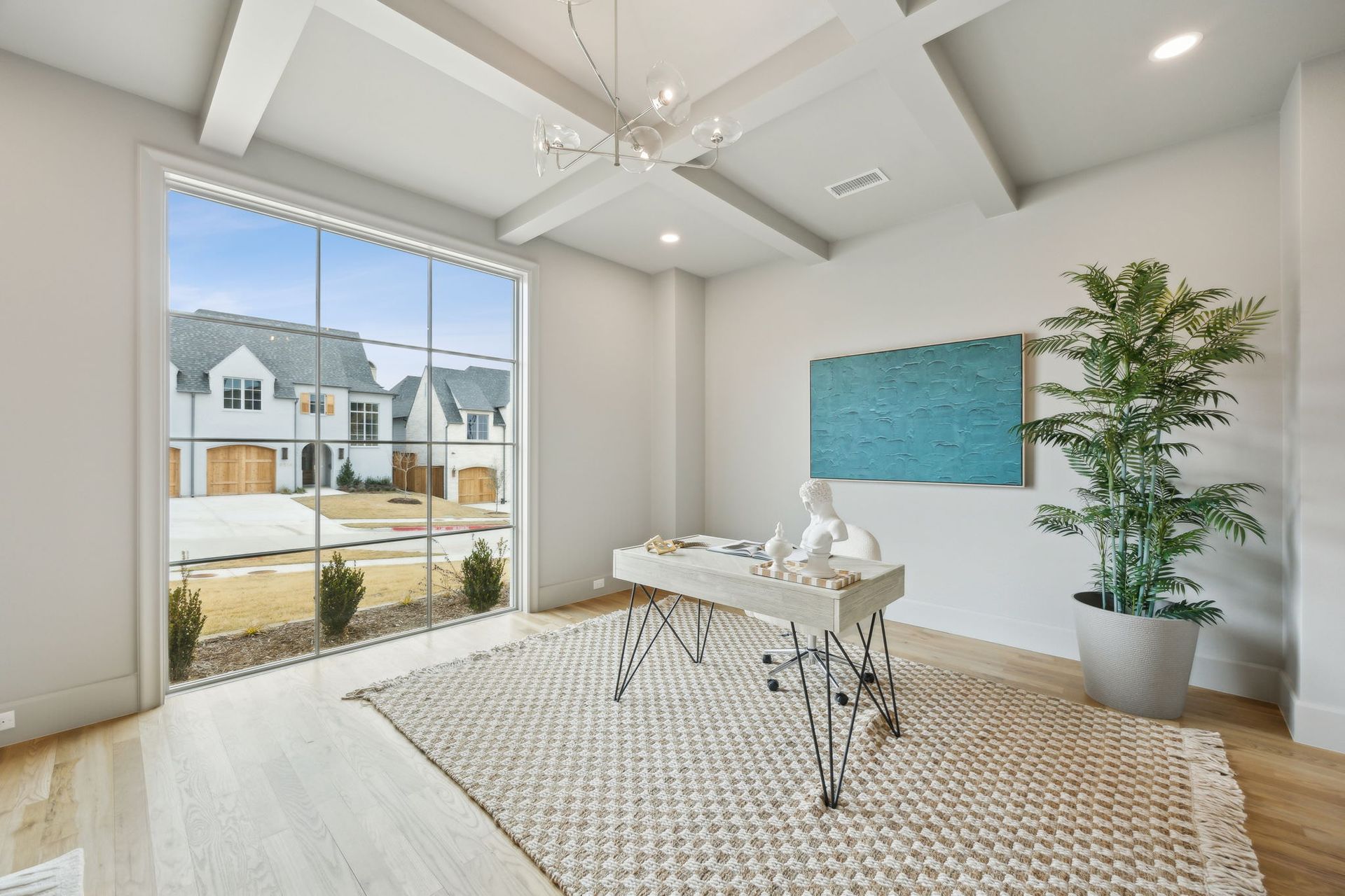 Bright home office with large window overlooking a neighborhood. Desk with decor, rug, and potted plant.