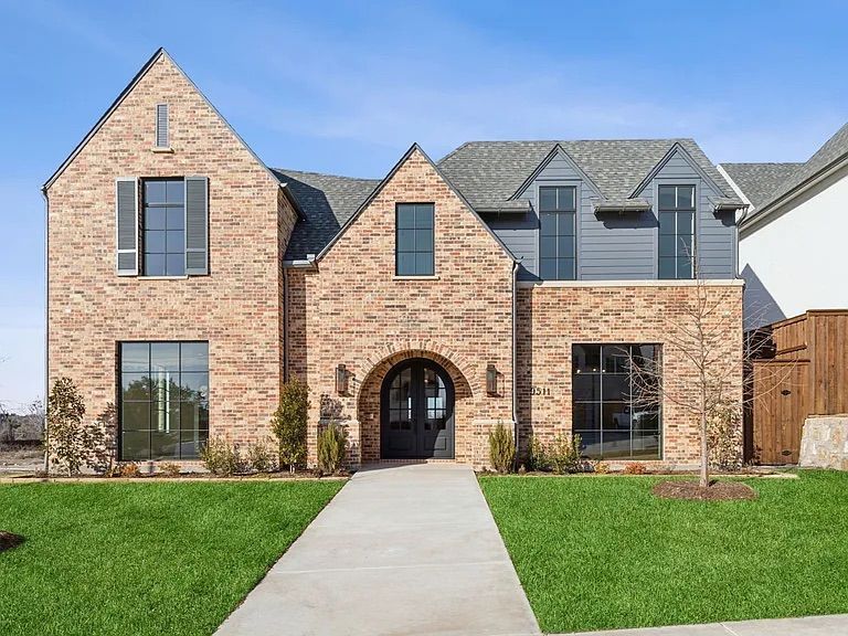 Brick home with gray roof and trim, arched doorway, and green lawn.