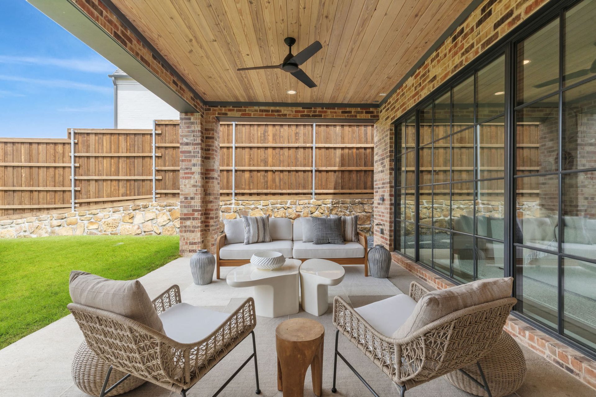 Patio with seating, brick walls, wood ceiling, and black framed glass door.