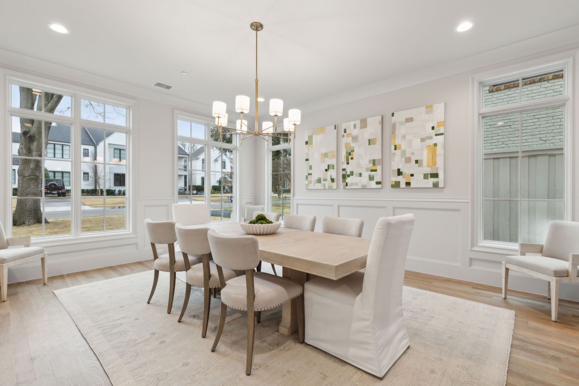 Dining room with table, chairs, large windows, chandelier, and white walls.