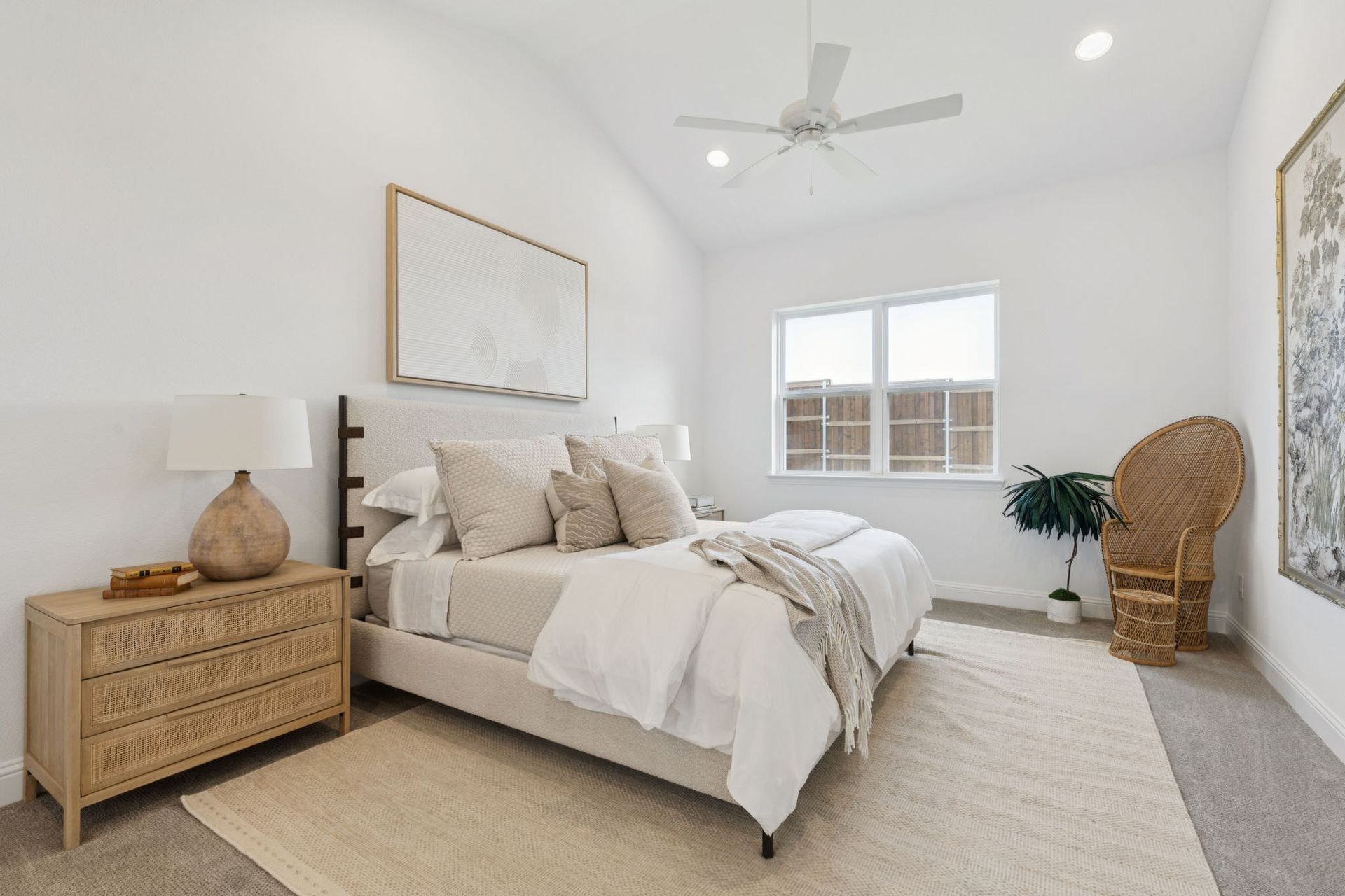 Bedroom with a bed, nightstand, art, wicker chair, and a window. Neutral tones create a calming space.