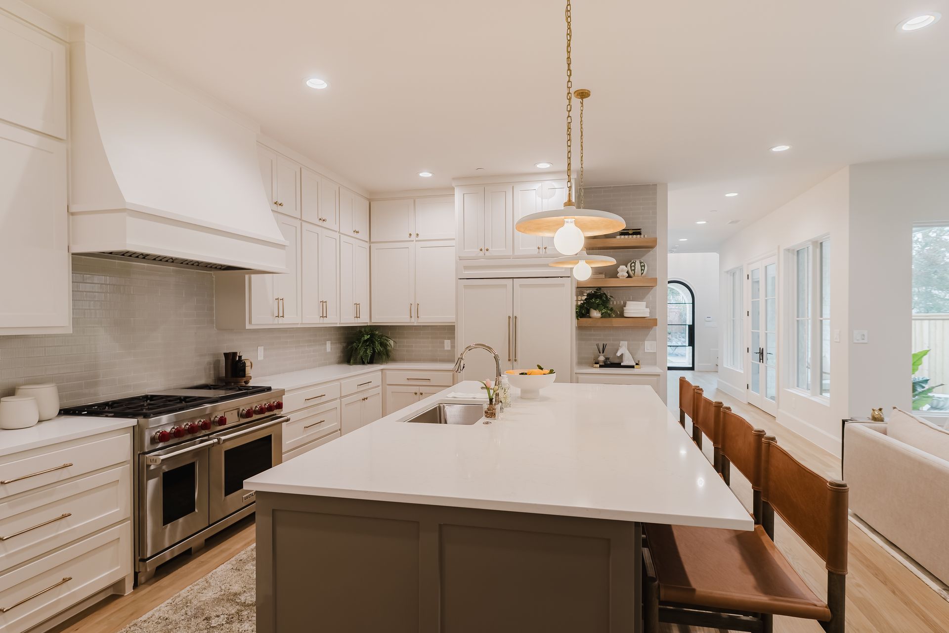 A kitchen with white cabinets , a large island , a stove , a refrigerator , and a sink.