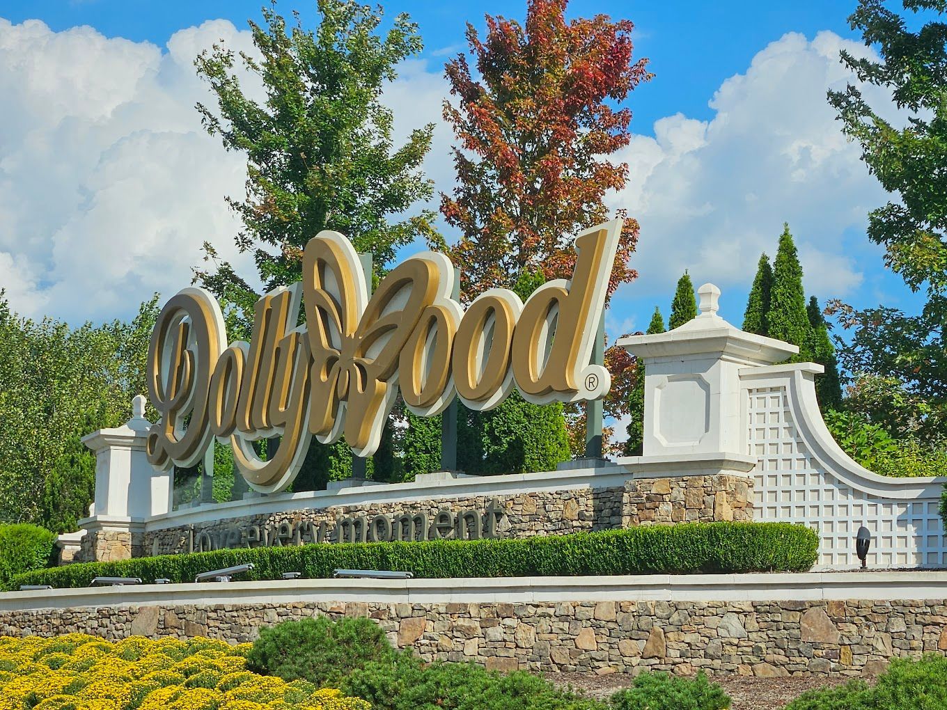 A sign for Dollywood is surrounded by trees and bushes