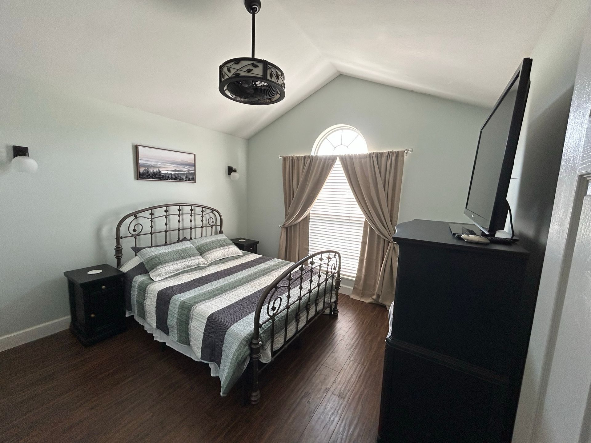 A bedroom with a bed , nightstand , television and a ceiling fan.