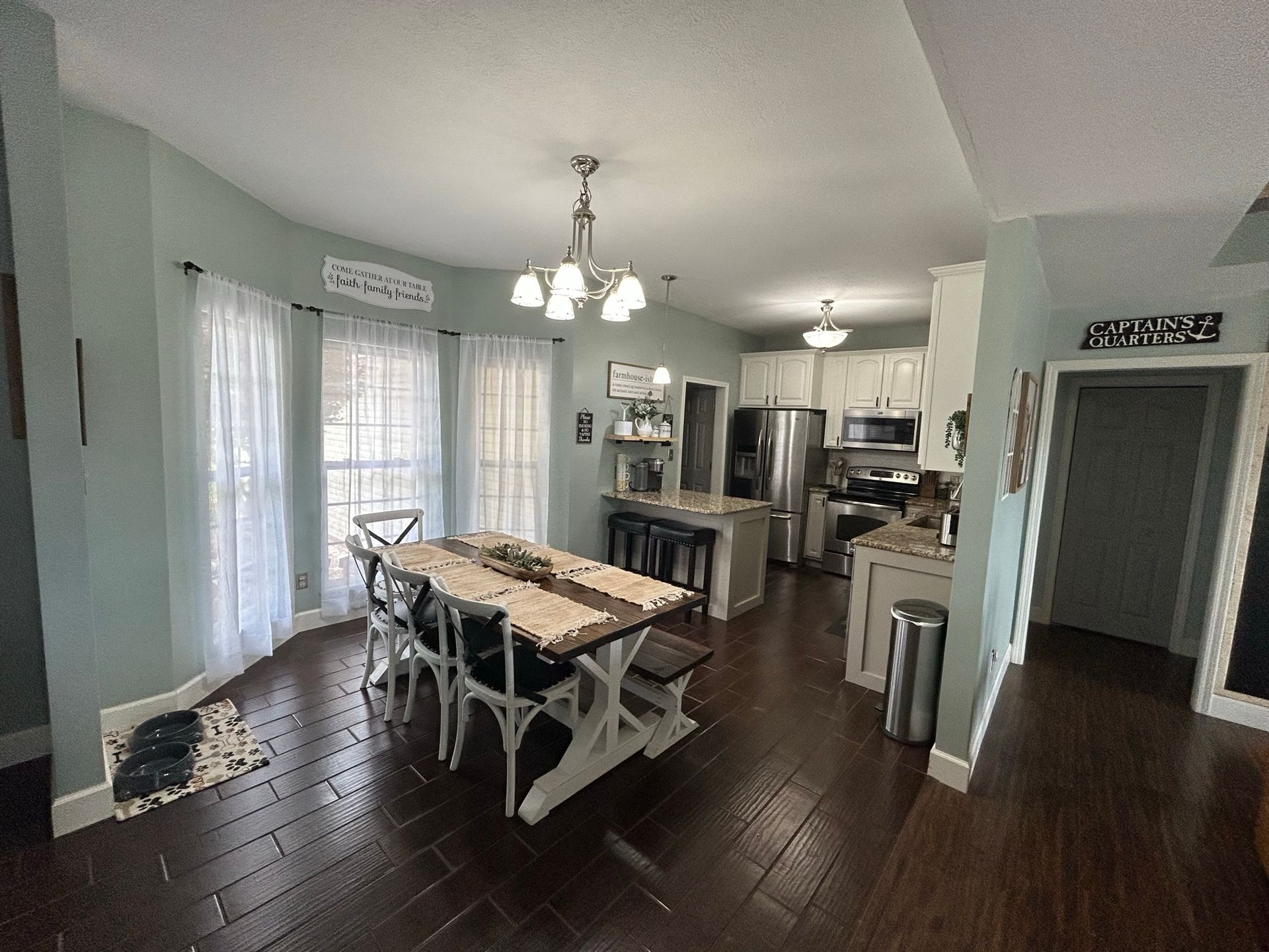 A dining room with a table and chairs and a kitchen in the background.