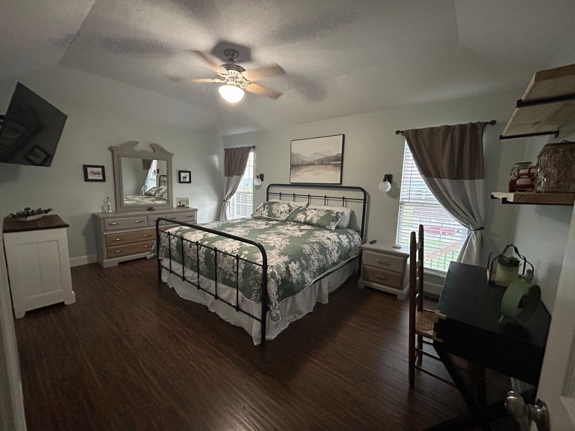 A bedroom with a king size bed , dresser , mirror and ceiling fan.