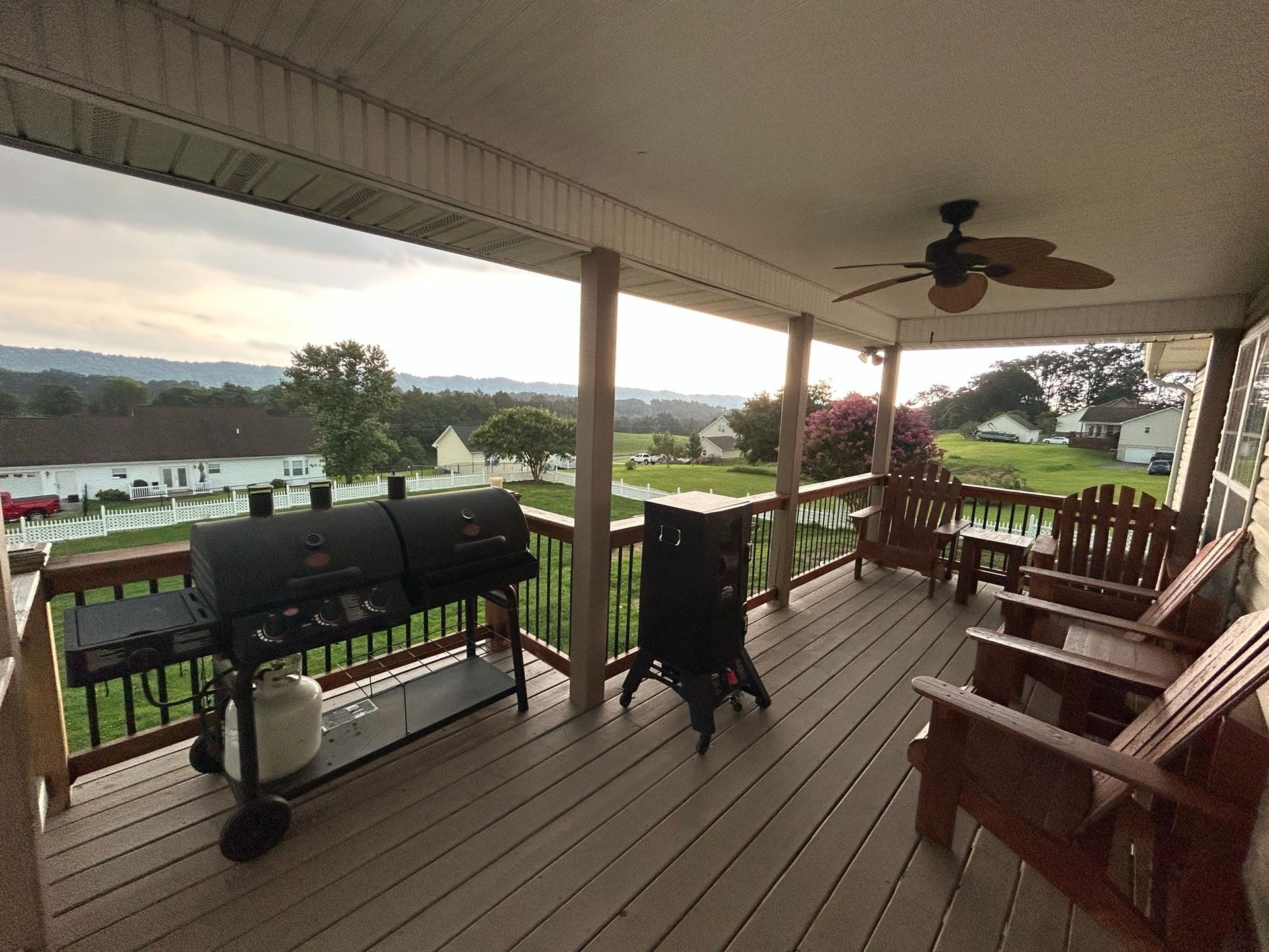 A porch with a grill and chairs and a ceiling fan