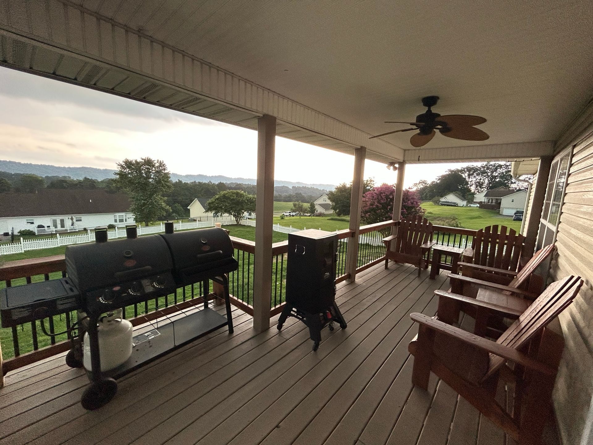 A porch with a grill and chairs and a ceiling fan