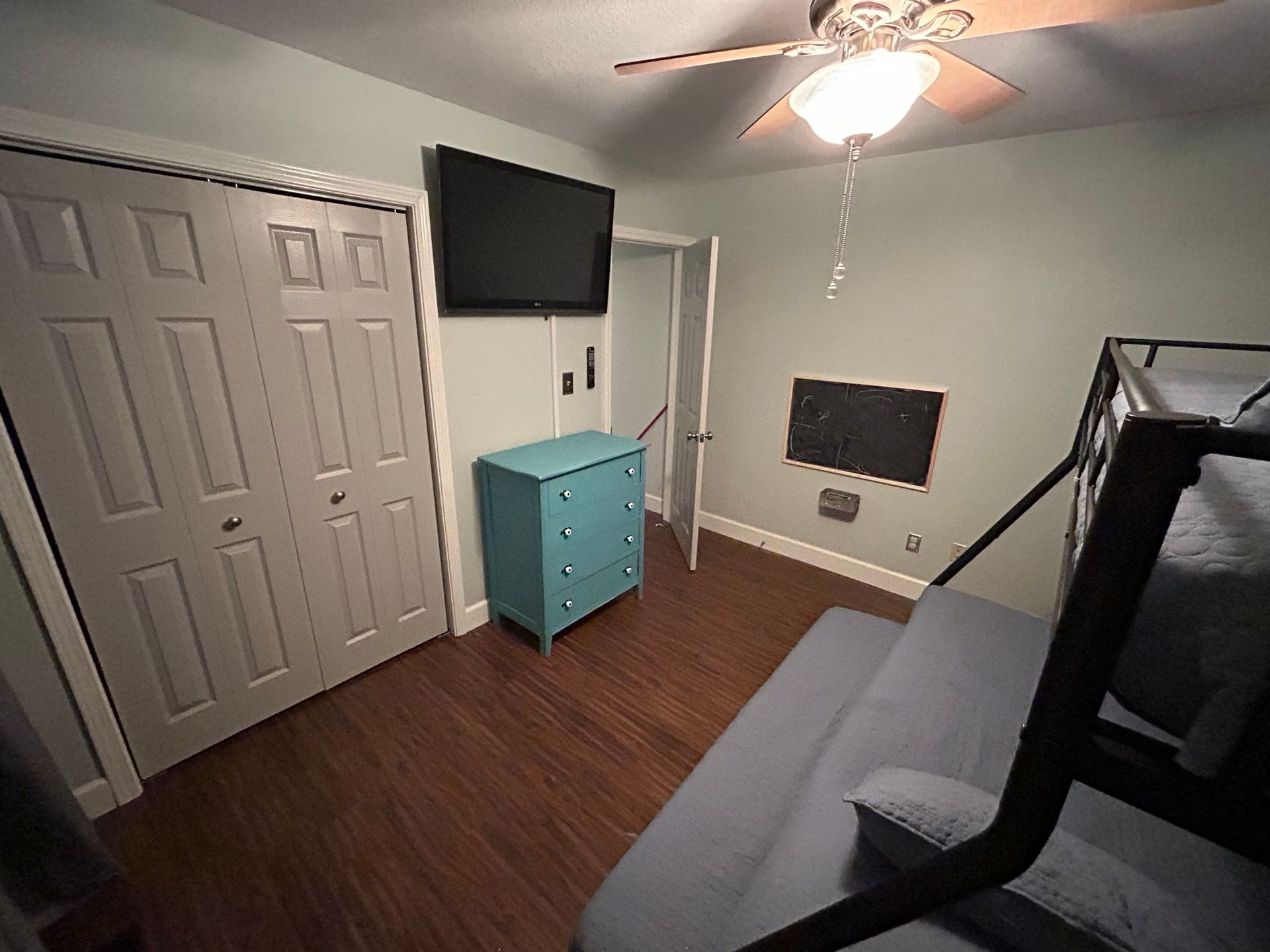 A bedroom with a bunk bed , dresser , television and ceiling fan.