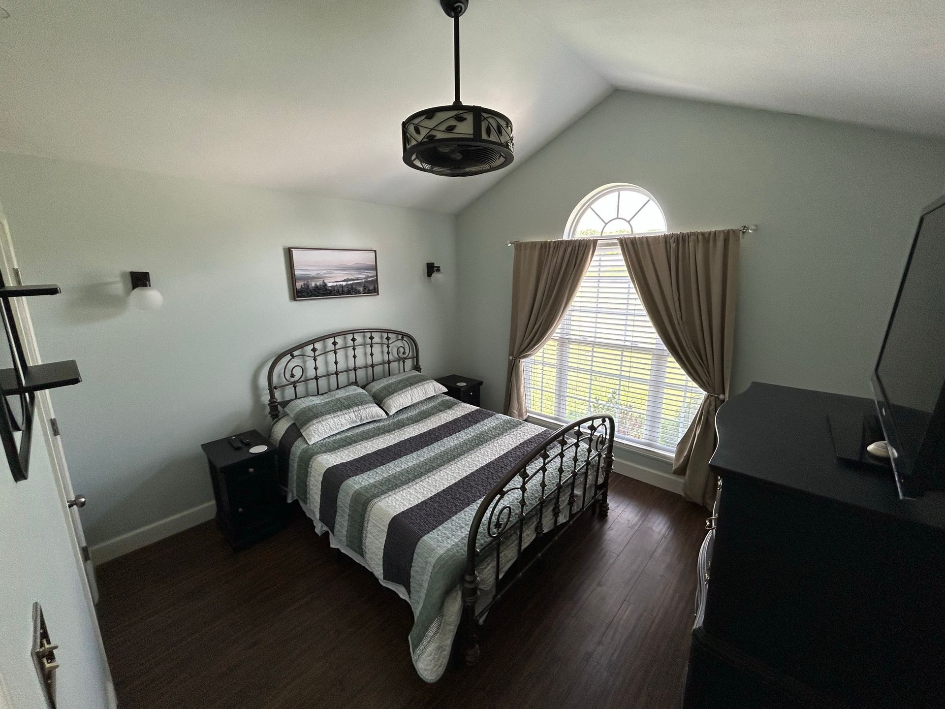 A bedroom with a bed , nightstand , television and ceiling fan.