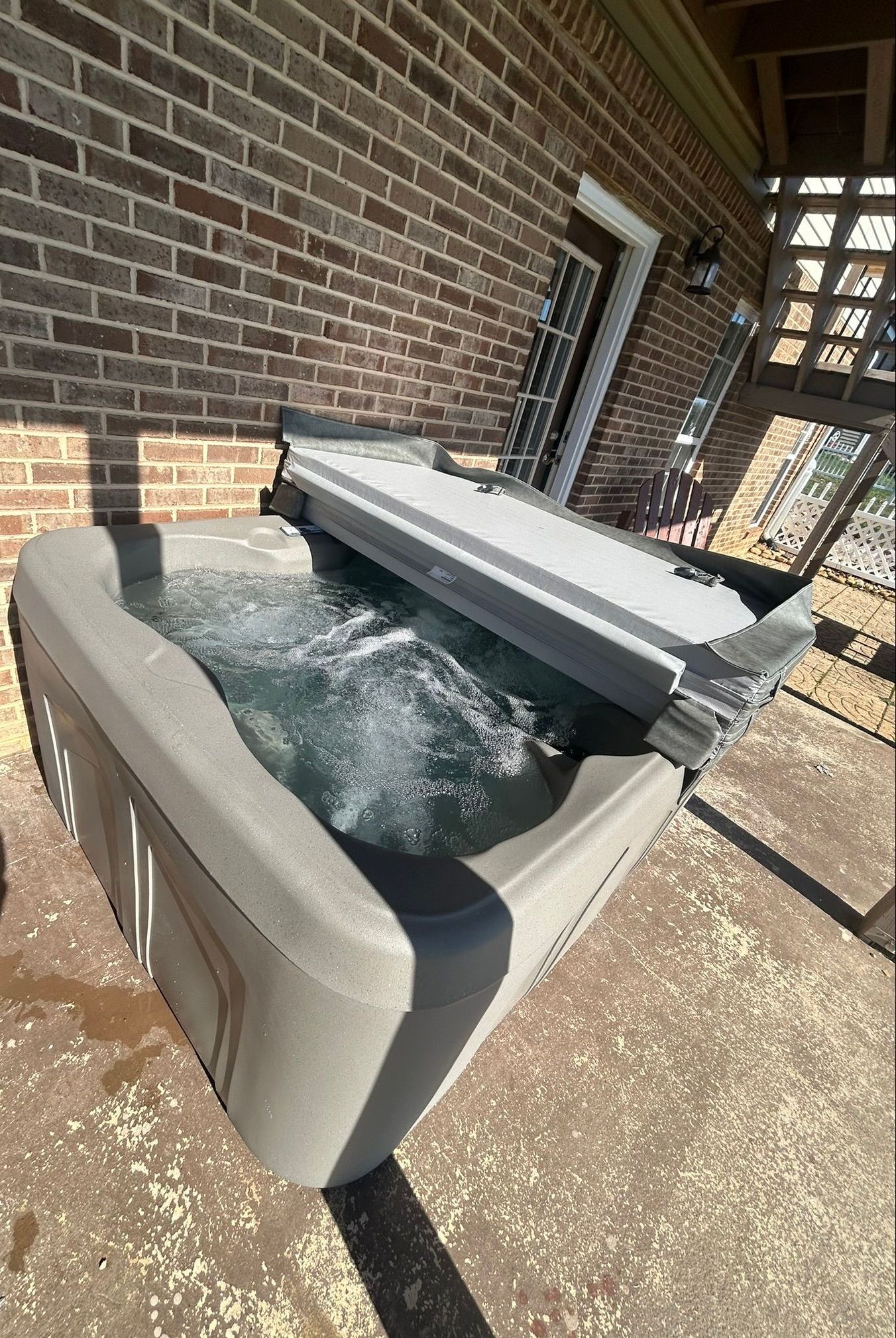 A hot tub is sitting on a patio in front of a brick building.