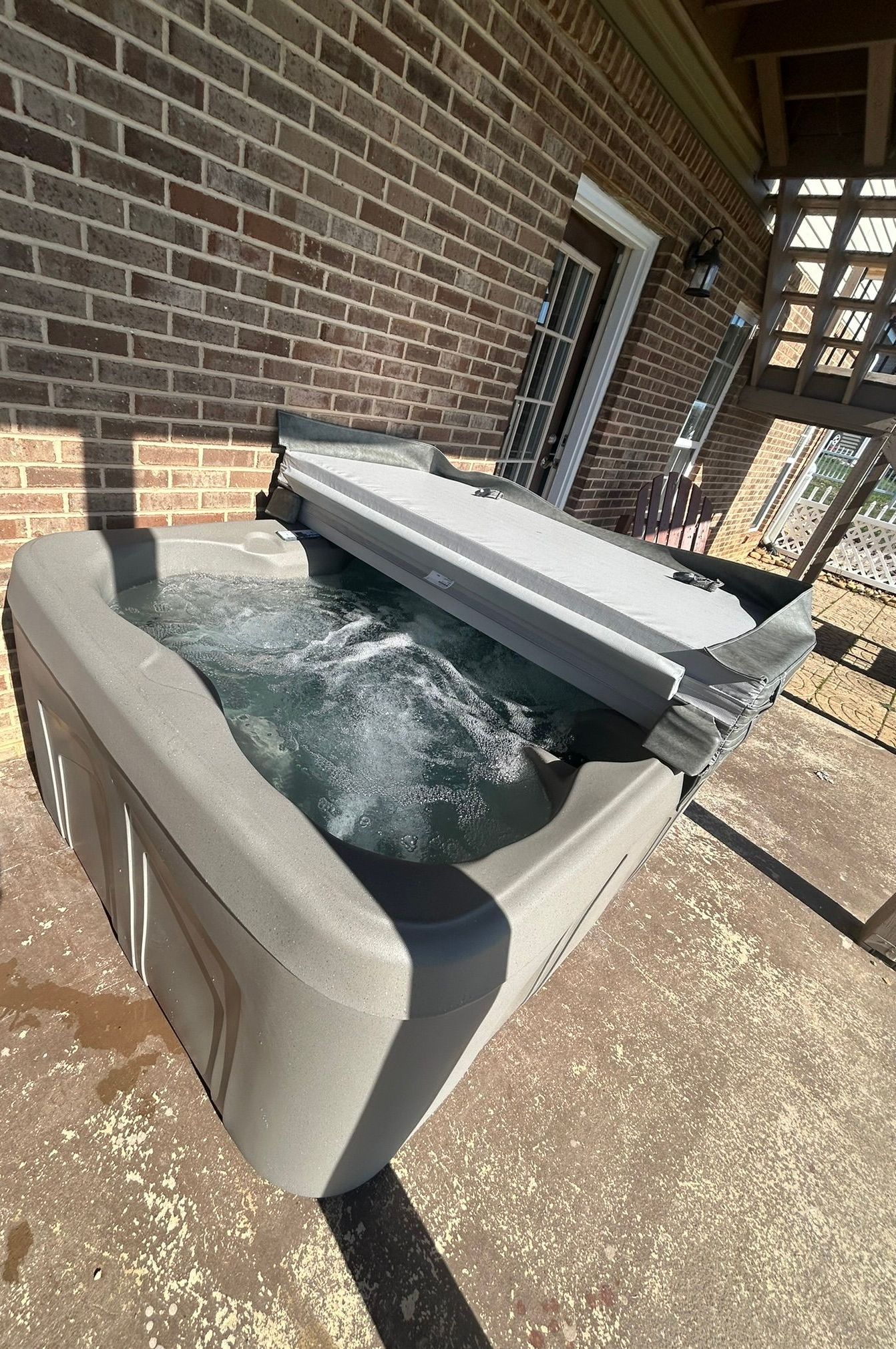 A hot tub is sitting on a patio in front of a brick building.