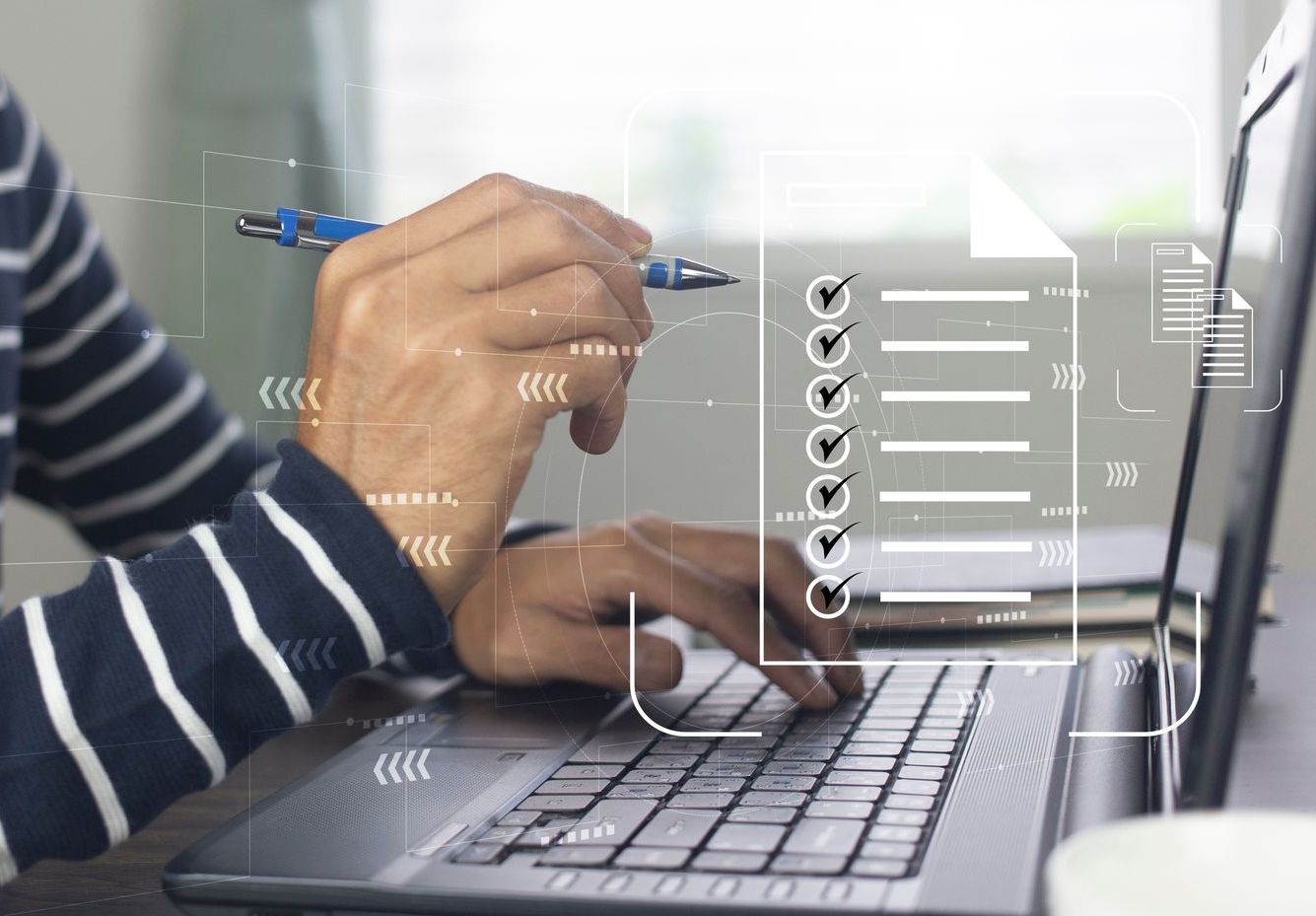 A person is typing on a laptop computer while holding a pen.