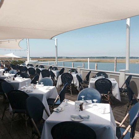 A restaurant with tables and chairs and umbrellas overlooking a body of water.