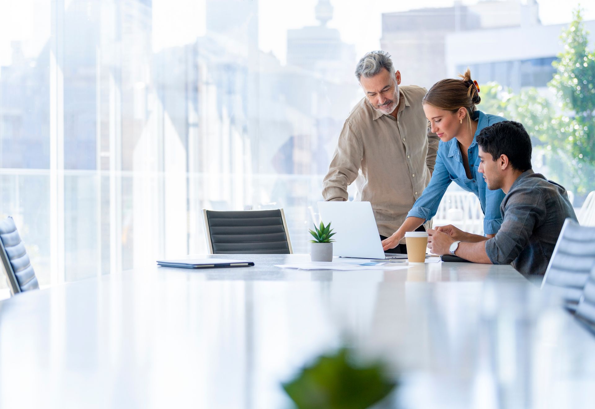 A group of people are sitting around a table looking at a laptop.
