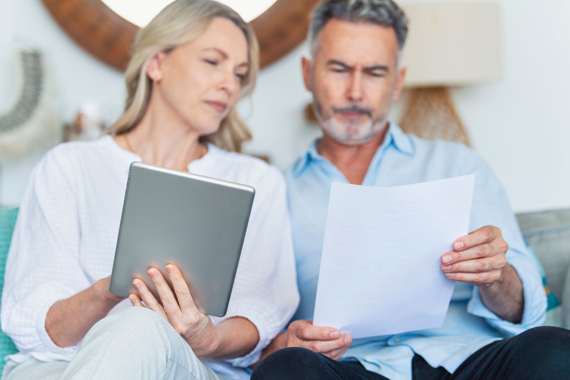 A man and a woman are sitting on a couch looking at papers and a tablet.