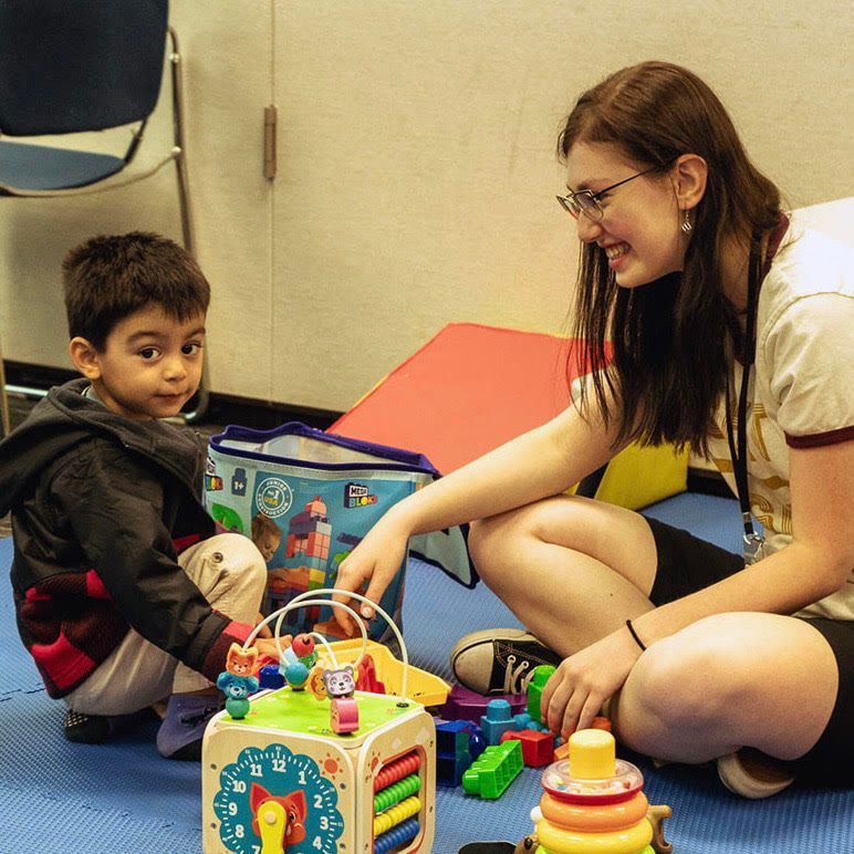 A woman sits on the floor with a child playing with toys