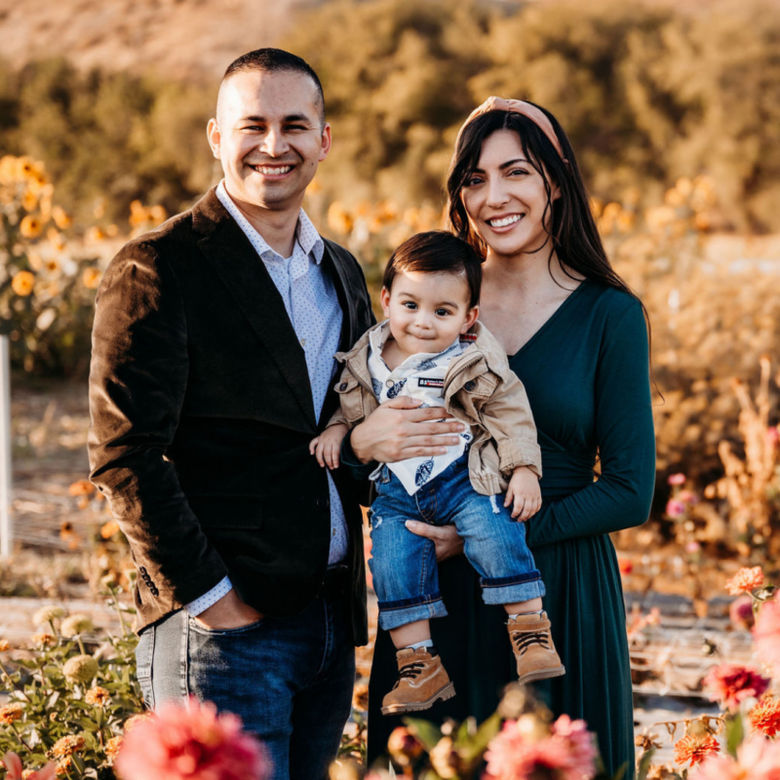 A man and woman are holding a baby in a field of flowers.