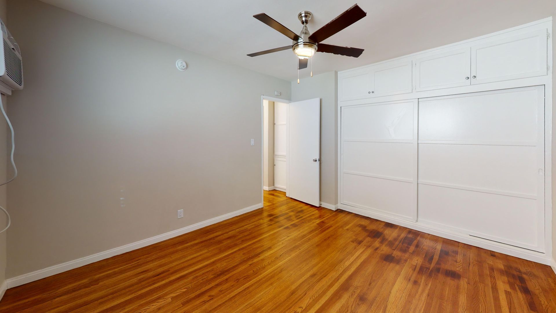 Empty bedroom with hardwood floors, white built-in cabinets, and a ceiling fan.