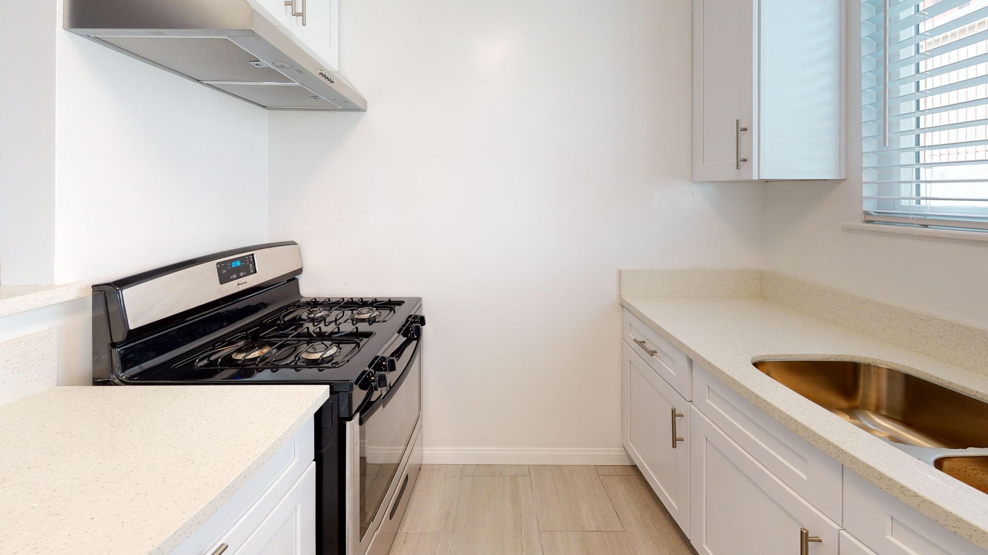 Bright, modern kitchen. Stainless steel range, white cabinets, light countertops, and a window with blinds.