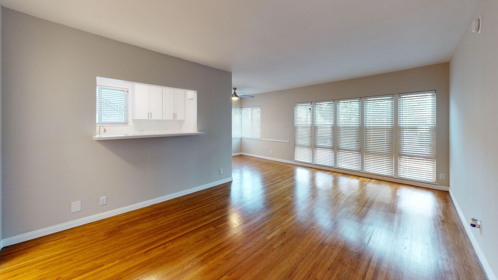 Empty living room with hardwood floors, large window, and wall-mounted cabinets.