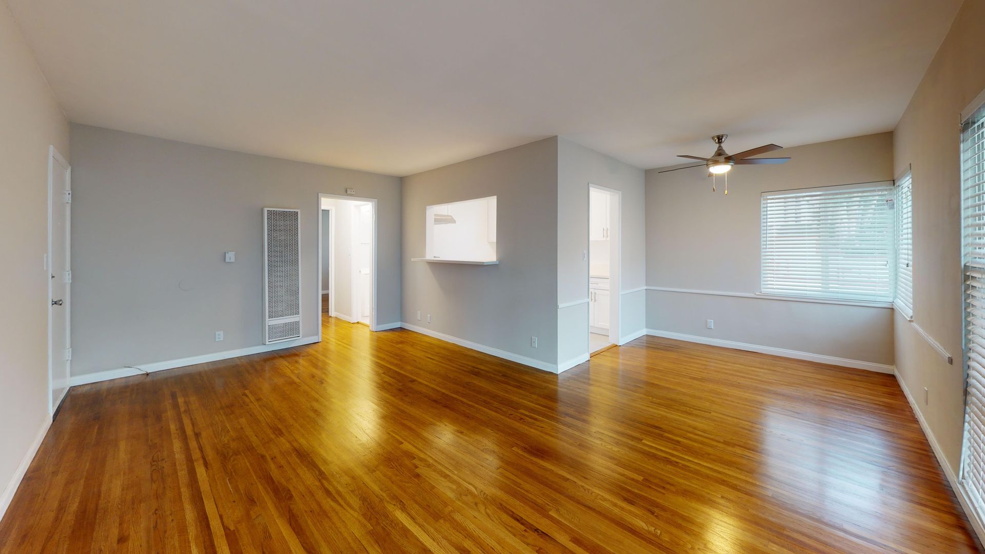 Empty living room with hardwood floors, light gray walls, and a ceiling fan.