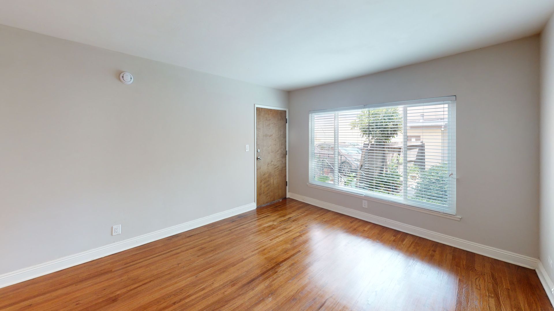 Empty room with hardwood floors, a window, and a closed door.