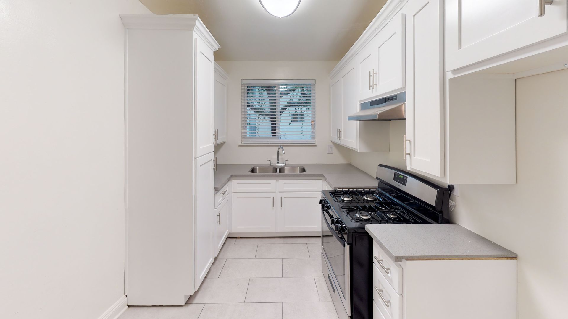 White kitchen with cabinets, stove, sink, and window.