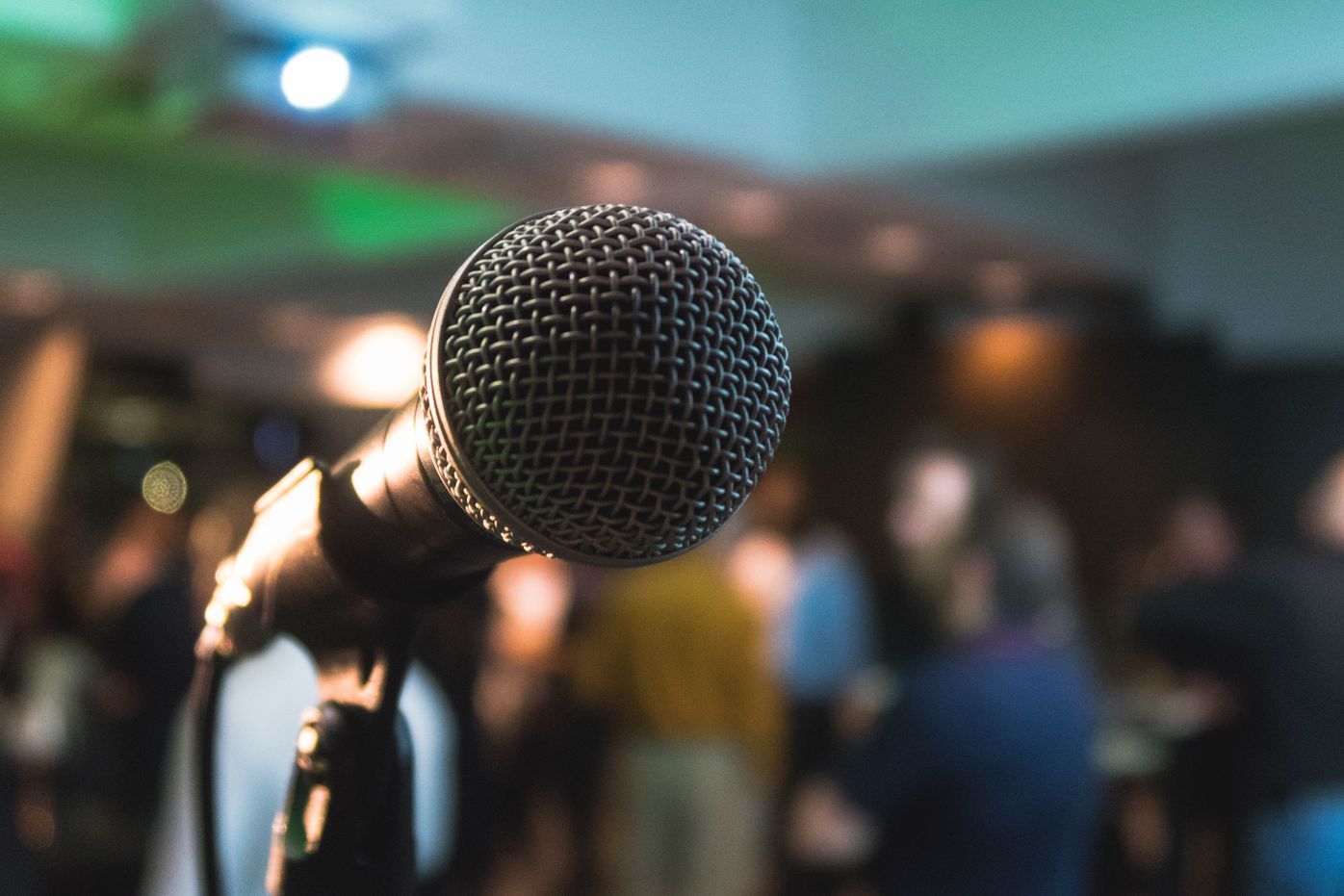 A microphone is sitting on a stand in front of a crowd of people.