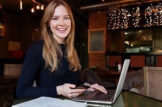 A woman is sitting at a table with a laptop and a cell phone.